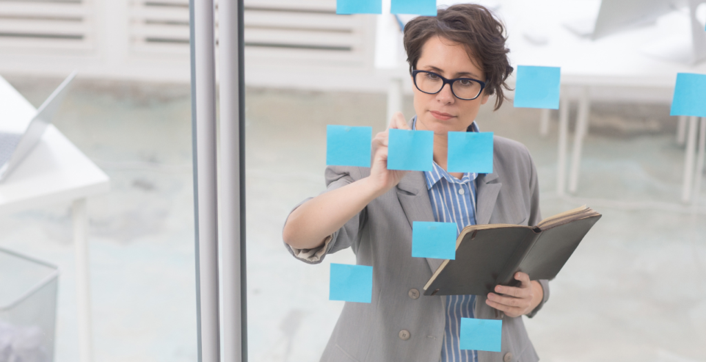 Woman putting blue sticky notes on window as she works to streamline medical practice operations